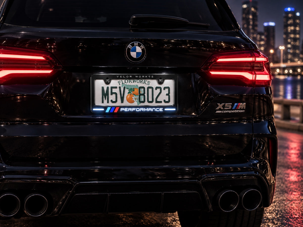 Velor Works Design B illuminated PERFORMANCE license plate frame on black BMW X5 M in city night scene