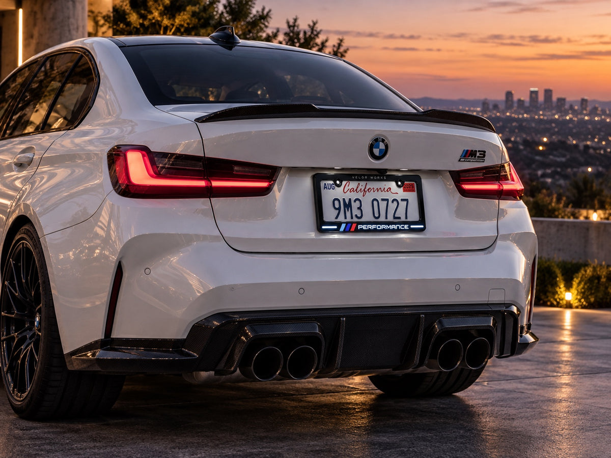 Velor Works Design B illuminated PERFORMANCE license plate frame on white BMW M3 at sunset