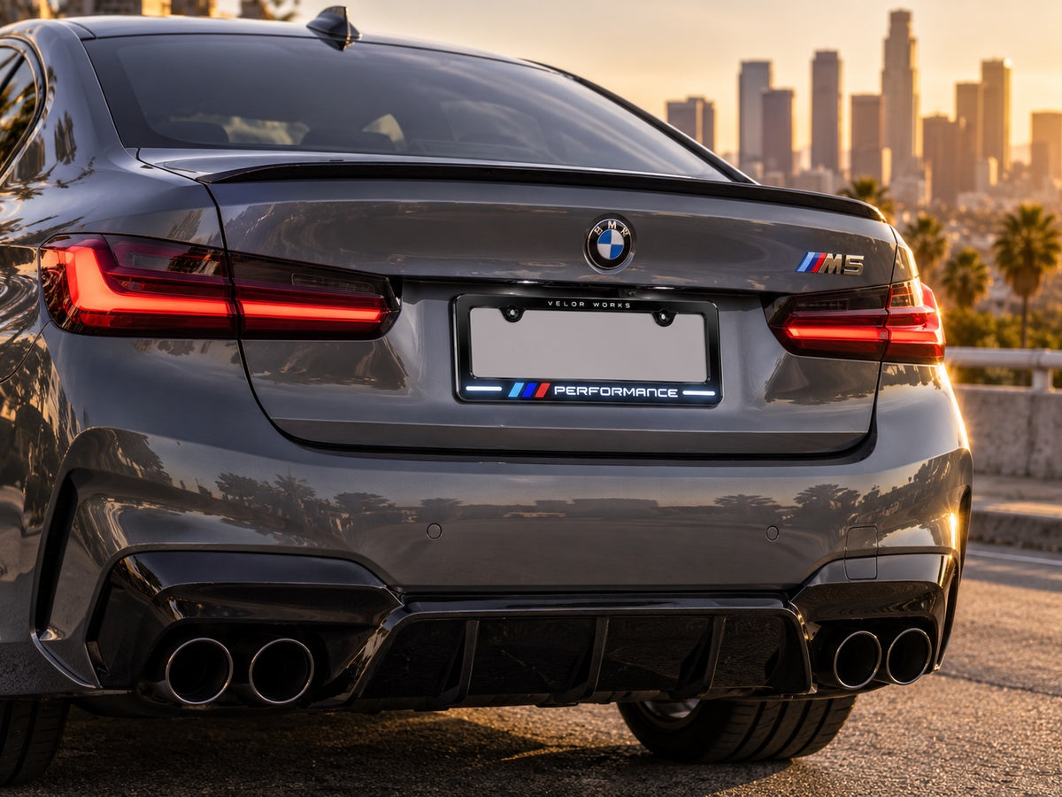 Velor Works Design B illuminated PERFORMANCE license plate frame on gray BMW M5 at sunset
