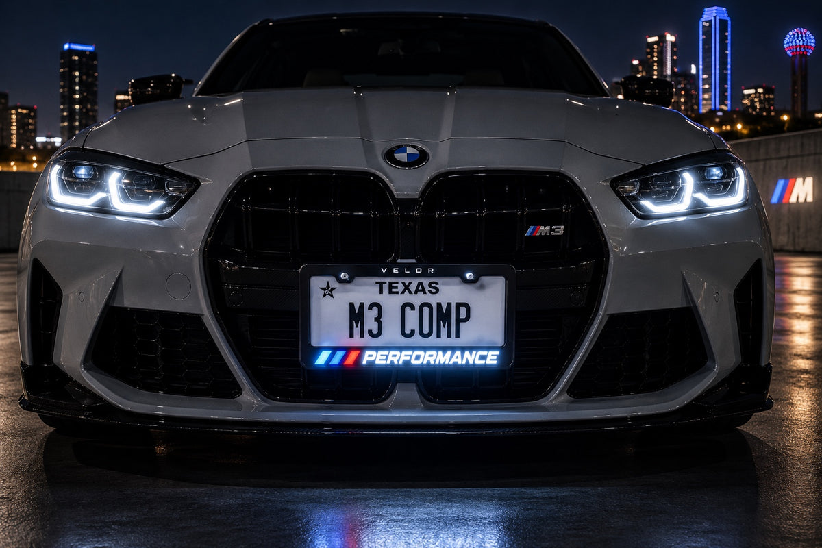 Velor Works illuminated PERFORMANCE license plate frame installed on a white performance sedan in a city night scene